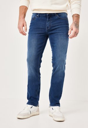 Blue denim jeans with slight fading, classic five-pocket design, straight fit, paired with white and gray sneakers on a light background.