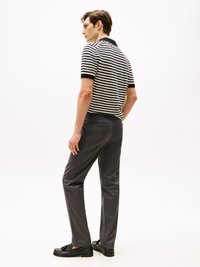 Schwarz-weiß gestreiftes kurzärmliges Poloshirt, taillierte graue Hose und schwarze Slipper. Glatte Textur und figurnahe Silhouette.