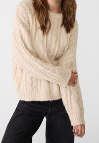 Pehmeäbeige neulottu villapaita, jossa pitkät hihat, resorit hihansuissa ja rento malli. Yhdistetty mustiin, hieman kuluneisiin farkkuihin.