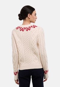 Pull en tricot crème avec motif floral rouge au niveau de l'encolure et des poignets, présentant une texture en maille torsadée et un ourlet côtelé.
