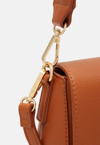 Borsa a mano in pelle marrone con texture a ciottoli, dotata di hardware dorato e tracolla removibile. Include un logo del marchio visibile sul gancetto.