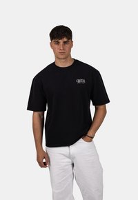 Zwarte katoenen t-shirt met korte mouwen en een ronde hals. Voorzien van een wit 'CRYSTAL' logo op de linkerborst. Te combineren met witte broeken.