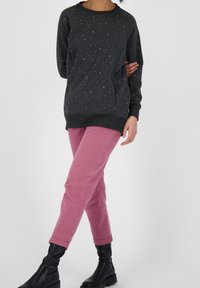 Sudadera gris con patrones triangulares multicolores, combinada con pantalones rosas; el modelo lleva botas negras hasta el tobillo; ajuste casual y textura suave.