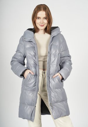 Manteau matelassé gris avec capuche, doté d'une finition brillante et texturée, d'une fermeture éclair et de poches latérales. Coupe ajustée avec coutures visibles.