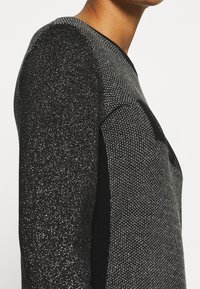 Pull noir et gris avec un motif texturé en fils métalliques, manches longues et encolure ronde.