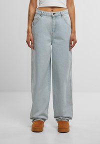 Jeans de pernera ancha en azul claro con cintura alta, con cierre de botón, diseño de cinco bolsillos y un ligero desvanecimiento. Combinados con calzado en tono marrón.