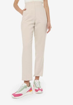 Pantaloni beige a vita alta con gambe dritte, tasche frontali, abbinati a sneakers multicolori con dettagli rosa, verde e bianco.