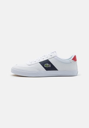 Sneaker bianco con una striscia diagonale navy, suola in gomma e logo ricamato verde. Presenta un accento rosso sul tallone e un design con lacci.