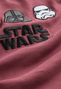Bordeauxrotes Baumwoll-T-Shirt mit gestickten Designs von Darth Vader und Sturmtruppen, versehen mit schwarzem Text, der in fetten Buchstaben "STAR WARS" liest.