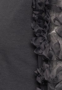 Tela de color gris oscuro que presenta un acento de encaje floral texturizado. Las flores están superpuestas y crean un efecto tridimensional a lo largo del borde.