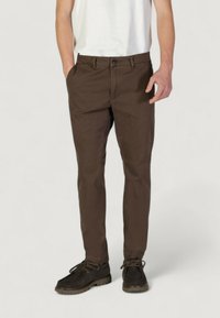 Chinos in cotone marrone con una vestibilità slim, caratterizzati da tasche frontali, zip con bottone e una texture liscia. Scarpe abbinate: marroni scuri con lacci.