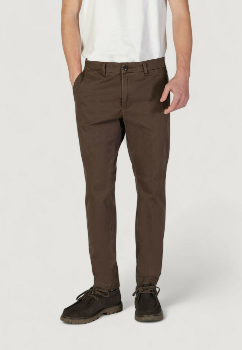 Chinos in cotone marrone con una vestibilità slim, caratterizzati da tasche frontali, zip con bottone e una texture liscia. Scarpe abbinate: marroni scuri con lacci.