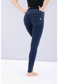 Leggings de mezclilla azul oscuro con cintura alta, que presentan una textura suave, bolsillos traseros triangulares y acentos de costura en tono dorado.