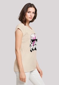 Beige short-sleeve t-shirt with a Stormtrooper graphic in black and pink. The shirt has a relaxed fit and a round neckline, made of soft fabric.
