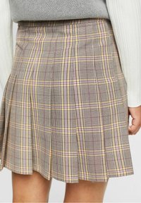 Falda de cuadros grises con pliegues, con líneas amarillas y rosas. Confeccionada en tela tejida con una textura suave. Visible la cintura y la parte trasera.