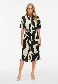 Svart-vit mönstrad skjortklänning i texturerat tyg, med knäppning fram, korta ärmar och ett bälte att knyta i midjan.
