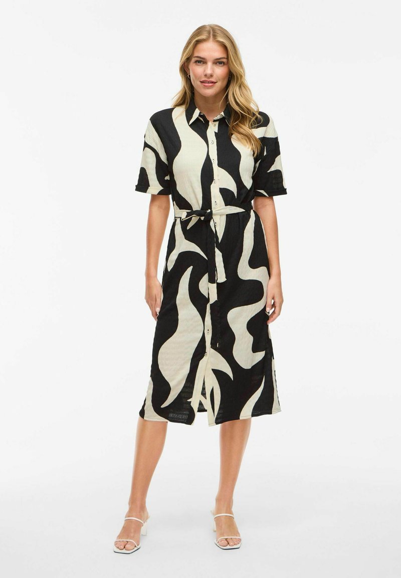 Svart-vit mönstrad skjortklänning i texturerat tyg, med knäppning fram, korta ärmar och ett bälte att knyta i midjan.