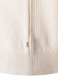 Kremowy sweter z dzianiny o prążkowanej fakturze, z metką po boku. Materiał wydaje się miękki i lekki.