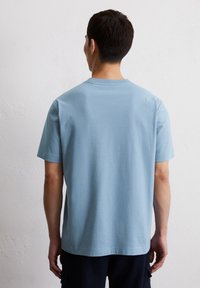Light blue cotton T-shirt with short sleeves, crew neckline, and a straight hem. Smooth texture, minimalistic design with no visible patterns.