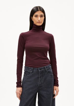 Burgunderfarbenes Langarm-Turtleneck-Oberteil aus glattem Stoff, kombiniert mit hochgeschnittenen, dunkelblauen weit geschnittenen Jeans. Schlichte Gestaltung, taillierter Schnitt.