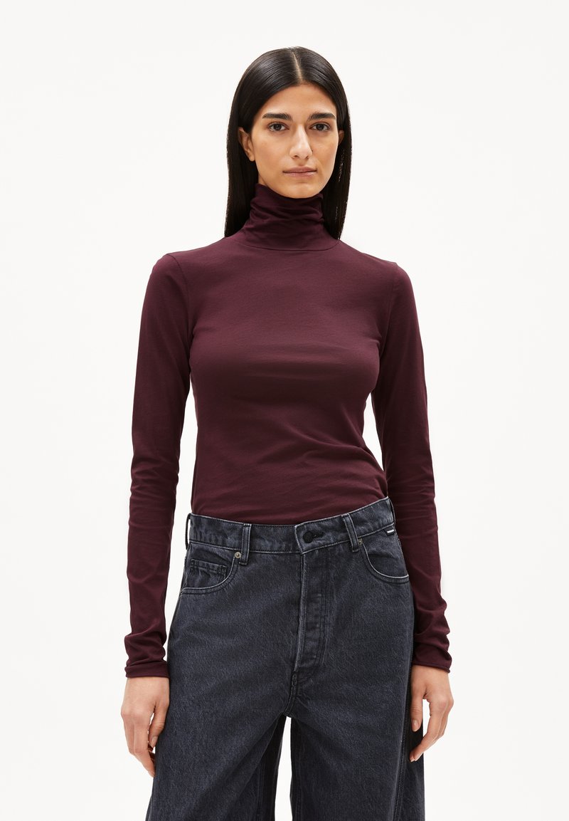 Burgunderfarbenes Langarm-Turtleneck-Oberteil aus glattem Stoff, kombiniert mit hochgeschnittenen, dunkelblauen weit geschnittenen Jeans. Schlichte Gestaltung, taillierter Schnitt.