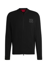 Sudadera negra con cremallera hecha de un material de punto suave. Presenta puños y dobladillo acanalados, con el logo "HUGO" en un tono oscuro contrastante en el pecho.