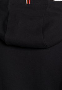 Sudadera con capucha negra de textura suave, con capucha negra y tres rayas paralelas en rojo, blanco y naranja cerca del cuello.