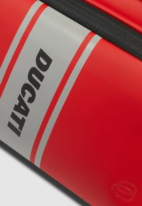 Rode tas met een matte afwerking, voorzien van een grijze streep en "DUCATI" duidelijk gedrukt in zwart. Inclusief een zwarte ritssluiting.