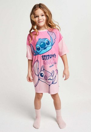 Young girl standing, wearing pink oversized nightshirt with Stitch and Angel characters from Lilo & Stitch.
