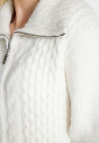 Giacca bianca con zip in tessuto testurizzato e soffice, con dettagli a coste sottili e una zip argentata sul colletto.