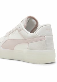 Vita och ljusrosa Puma-sneakers som visar sida och baksidan med mocka- och lädertexturer samt synlig Puma-logotyp på häl och sida.