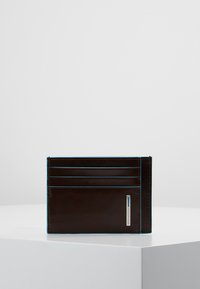 Tarjetero de piel marrón con cuatro ranuras para tarjetas, adornos de tejido azul y una placa de marca plateada. Textura suave, forma rectangular.