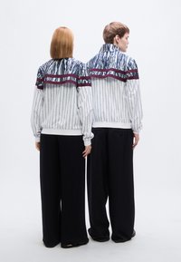 Δύο άτομα φορούν μπουφάν με σχέδιο μπλε και λευκές ρίγες, που περιλαμβάνει μια μαροκινή ζώνη, σε συνδυασμό με μαύρο παντελόνι με φαρδιά πόδια.