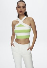 Top corto a fascia a righe verdi e bianche con spalline incrociate; modello abbinato a pantaloni sartoriali bianchi. Tessuto a maglia liscia.