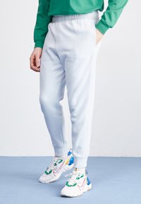 Ljusblå sweatsbyxor med elastisk midja och sidofickor. En vit Nike-logga syns på vänster lår, i kombination med färgglada sneakers.