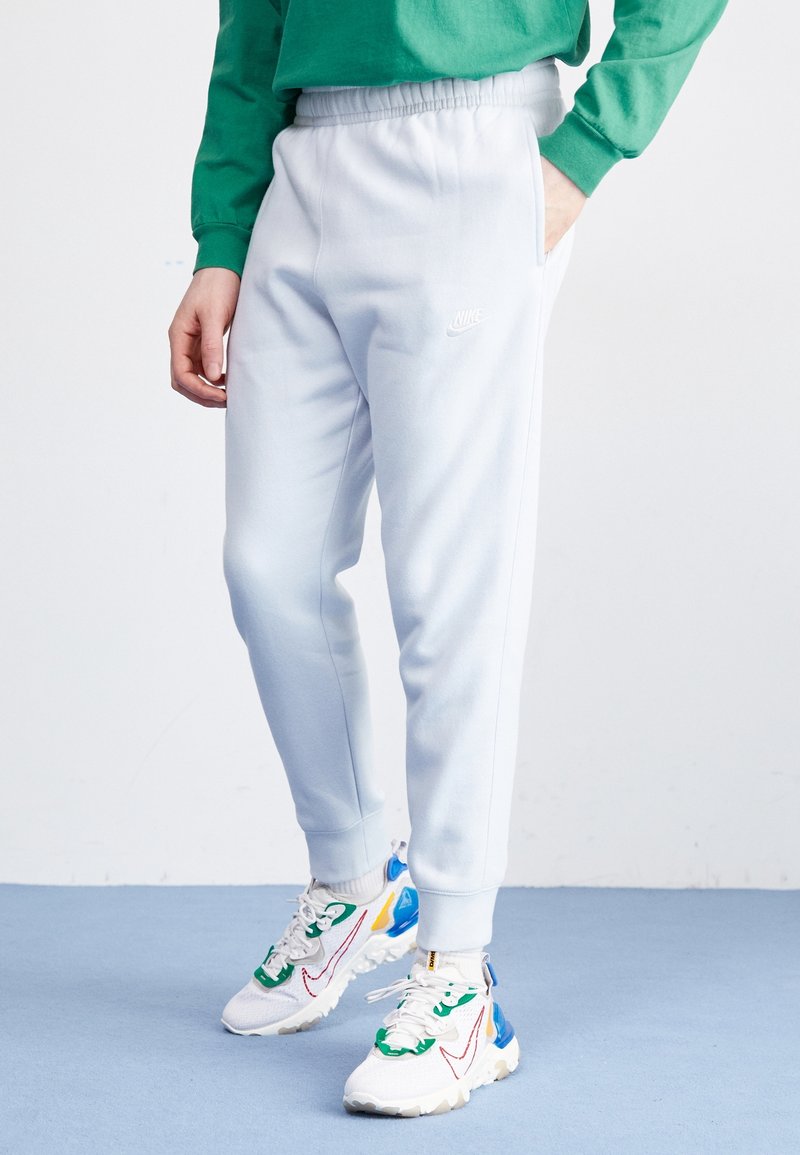 Ljusblå sweatsbyxor med elastisk midja och sidofickor. En vit Nike-logga syns på vänster lår, i kombination med färgglada sneakers.