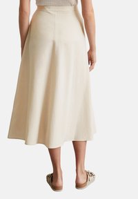Beige cotton midi skirt with a smooth texture, flared silhouette, and a mid-rise waistband, paired with tan slide sandals.