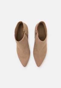 Beige ruskindsankelstøvler med spidse tæer og lynlåse i siden. Glat overflade, minimal syning og diskret branding indeni.