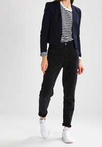 Svarta högmidjade jeans som matchas med en marinblå kort kavaj över en vit- och marinrandig skjorta, kompletterat med vita sneakers.