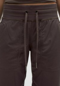 Pantaloni sportivi maro cu un tiv ribflat, șnururi ajustabile, două buzunare laterale și o textură de țesătură netedă și sleek.