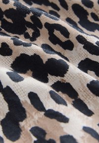 Tessuto a stampa leopardata con grandi macchie nere e marrone chiaro su uno sfondo beige chiaro, con una texture morbida e dettagli della trama visibili.