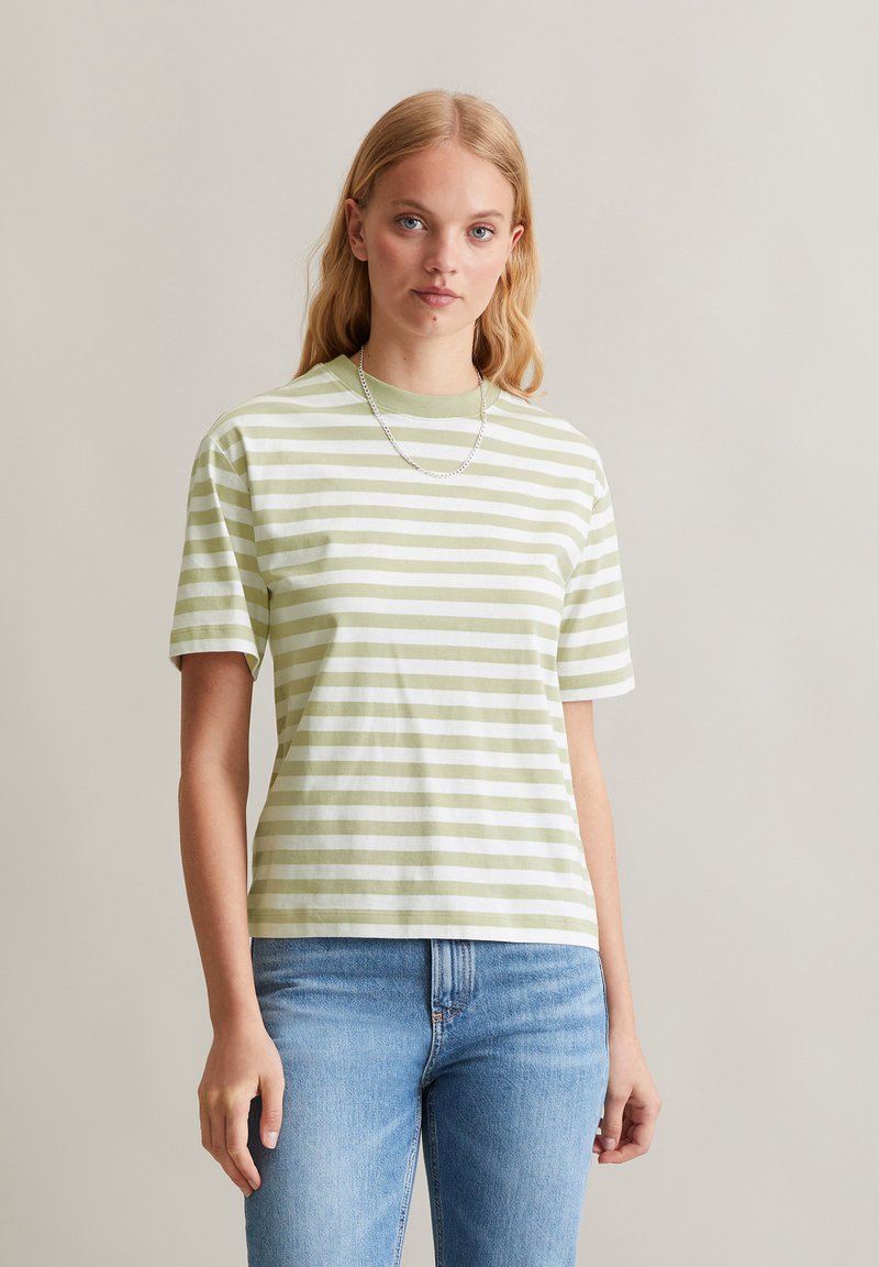 T-shirt rayé en vert pâle et blanc, fabriqué en coton doux, avec des manches courtes et un col rond, associé à un jean bleu clair.