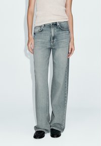 Světle šedé džíny s širokými nohavicemi a vysokým pasem, vyrobené z denimu, s pěti kapsami, jemným vydřením a klasickým zapínáním na knoflík.