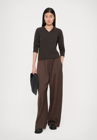 Barna V-kivágású pulóver, deréknál testhezálló, széles lábú barna nadrággal párosítva. A fekete clutch táska és cipők teszik teljessé az öltözetet.