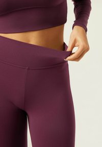 Maroon athletic top and leggings with a fitted design. Leggings feature a high waistband and a side pocket for convenience.