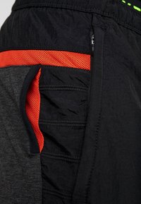 Schwarze Sportshorts mit orangefarbenen Mesh-Details, Reißverschluss-Tasche und strukturiertem Stoff. Mit glattem Bund und schlankem Design.