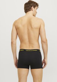 Schwarze Boxershorts mit eng Sitz, featuring ein gelbes "JACK & JONES"-Logo am Bund. Glattes Material und minimales Design.