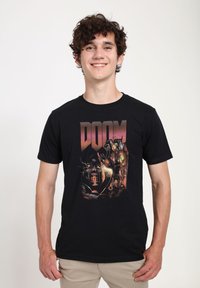Černé bavlněné tričko s grafickým designem, na kterém je slovo "DOOM" tučnými, stylizovanými písmeny a složitými ilustracemi postav a prvků.