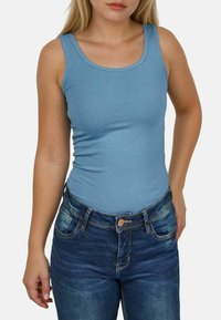 Blauwe mouwloze tanktop van zachte stof, gecombineerd met mid-rise donkerblauwe jeans met zakken en een knoopsluiting.