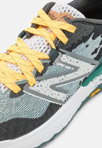 Black, grey, and teal running shoe with a mesh upper, yellow laces, and a textured sole. Features a prominent logo on the side.